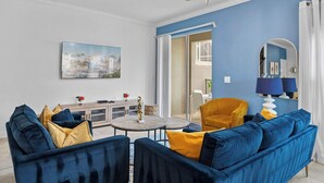 A living room with a blue sofa, a yellow armchair, a round coffee table, and a chandelier. - Gorgeous 5bed TH Close to Disney, Water Park (Davenport)