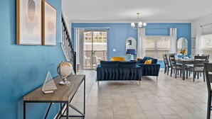 A living room with a blue wall, a sofa, a dining table with chairs, and a staircase. - Gorgeous 5bed TH Close to Disney, Water Park (Davenport)