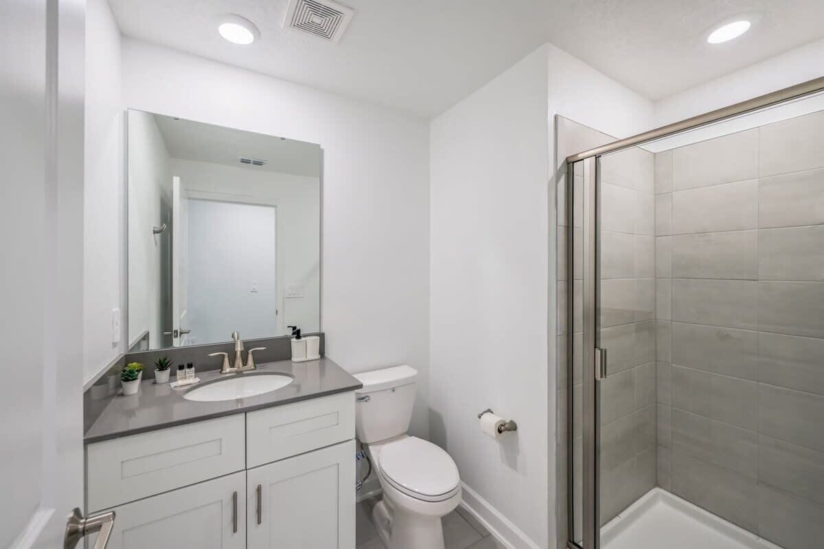 A modern bathroom with a glass shower enclosure, a white sink, and a large mirror.