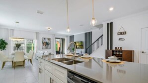 A modern kitchen with a central island, stainless steel appliances, and a dining area with a white table and chairs. - Opulent Retreat Themed Bedrooms and Pool Paradise (Kissimmee)