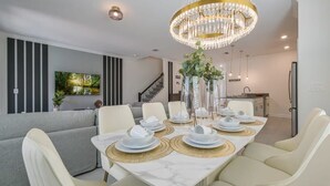 A dining area with a marble table, white chairs, gold placemats, and a chandelier. - Opulent Retreat Themed Bedrooms and Pool Paradise (Kissimmee)