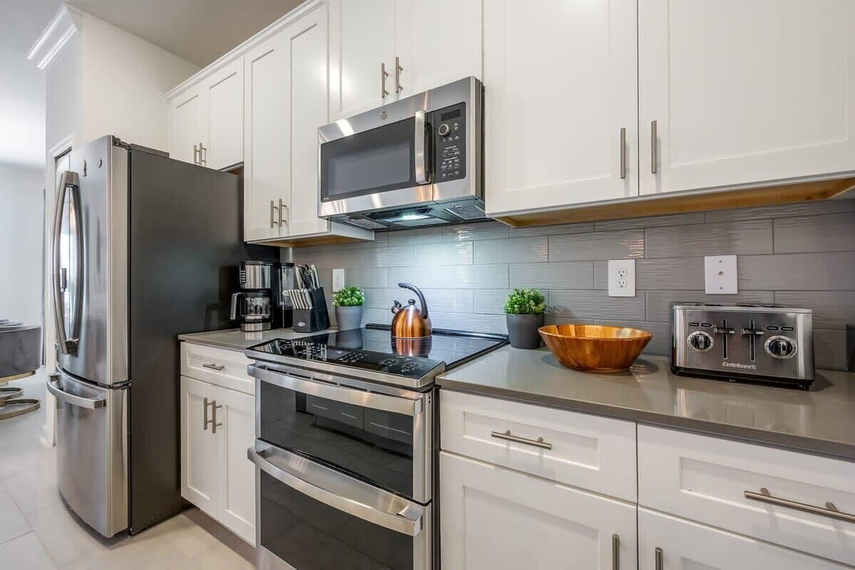 Una cocina moderna con electrodomésticos de acero inoxidable, armarios blancos y salpicadero de azulejos.
