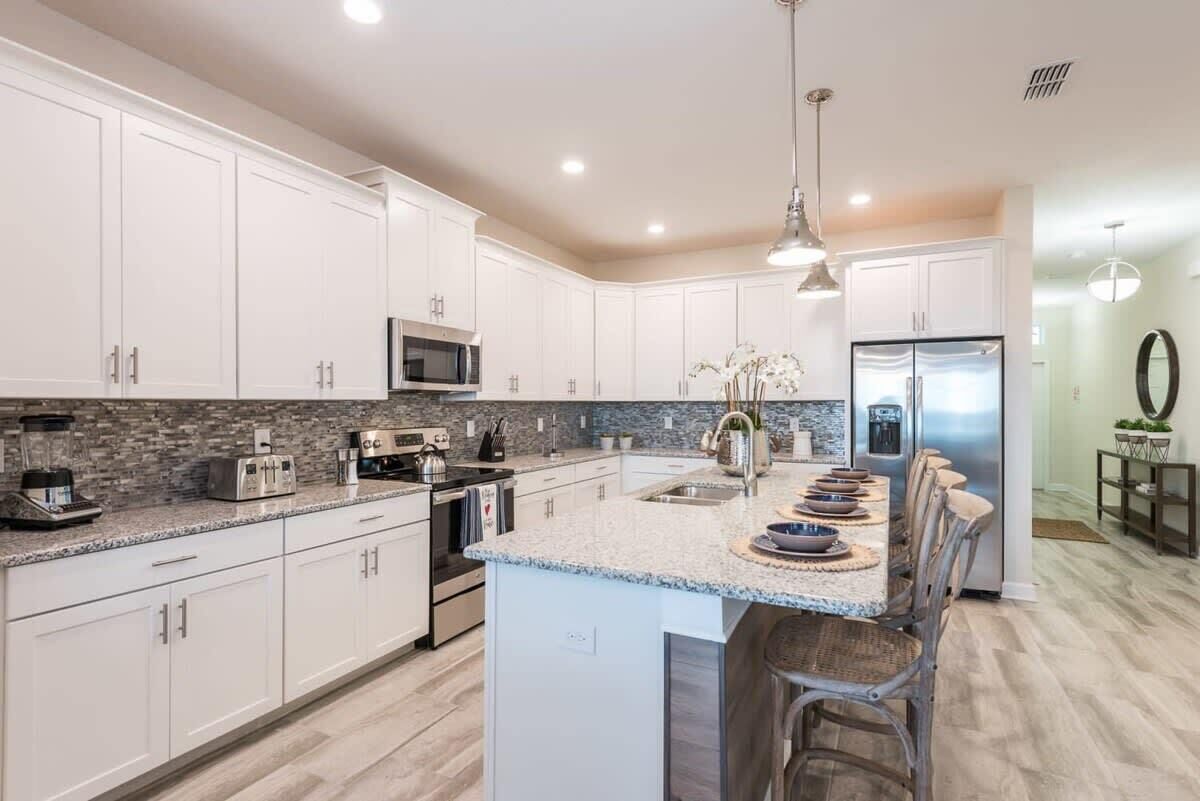 A modern kitchen with white cabinets, granite countertops, stainless steel appliances, and a central island with bar stools.