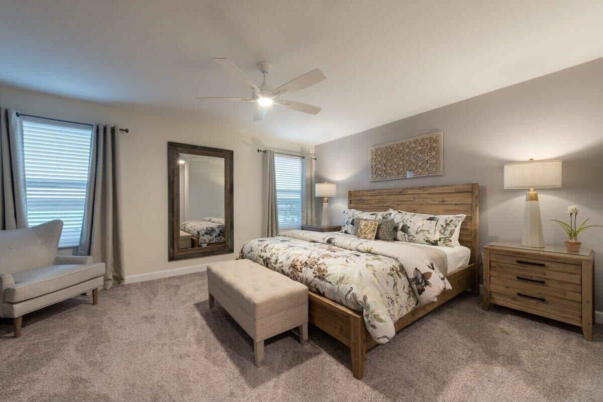 A bedroom with a bed, a nightstand, a chair, a mirror, and a ceiling fan.