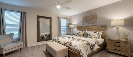 A bedroom with a bed, a nightstand, a chair, a mirror, and a ceiling fan.