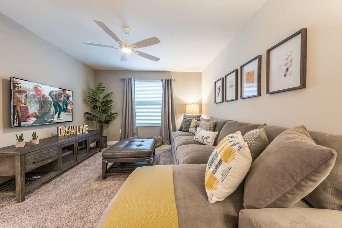 Ein Wohnzimmer mit einer Couch, einem Couchtisch, einem Fernseher, einem Deckenventilator und gerahmten Kunstwerken an der Wand.