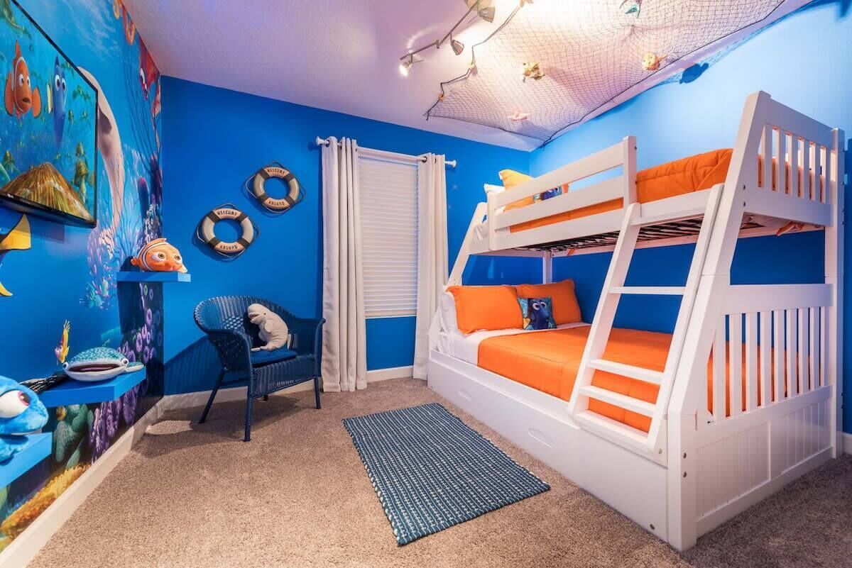 Una cama litera con ropa de cama naranja, una silla azul, un estante con juguetes y un mural en la pared.