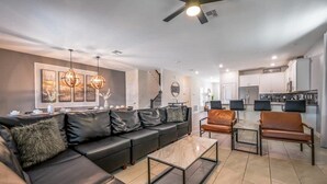 A modern living room with a sectional sofa, a coffee table, and a dining area with chairs. - Family Paradise, Space, Themed, Perfect Location (Kissimmee)