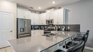 A modern kitchen with white cabinets, stainless steel appliances, a large island with seating, and a tiled backsplash. - Family Paradise, Space, Themed, Perfect Location (Kissimmee)