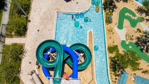 An aerial view of a water park with a large water slide, a swimming pool, and a sandy area with lounge chairs. - Family Paradise, Space, Themed, Perfect Location (Kissimmee)