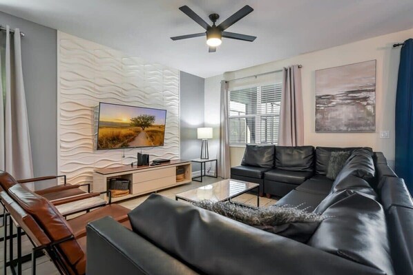 Een moderne woonkamer met een bank, salontafel, televisie en decoratieve wand.