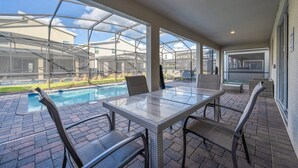 A covered patio with a glass table and chairs, a brick floor, and a view of a swimming pool and houses. - Family Paradise, Space, Themed, Perfect Location (Kissimmee)