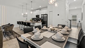 A modern kitchen with white cabinets, a central island, and a dining area with a long table set for six. - Modern Design Near Disney Top Resort (Kissimmee)