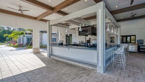 A modern outdoor bar area with a counter, bar stools, ceiling fans, and a view of the garden. - Modern Design Near Disney Top Resort (Kissimmee)