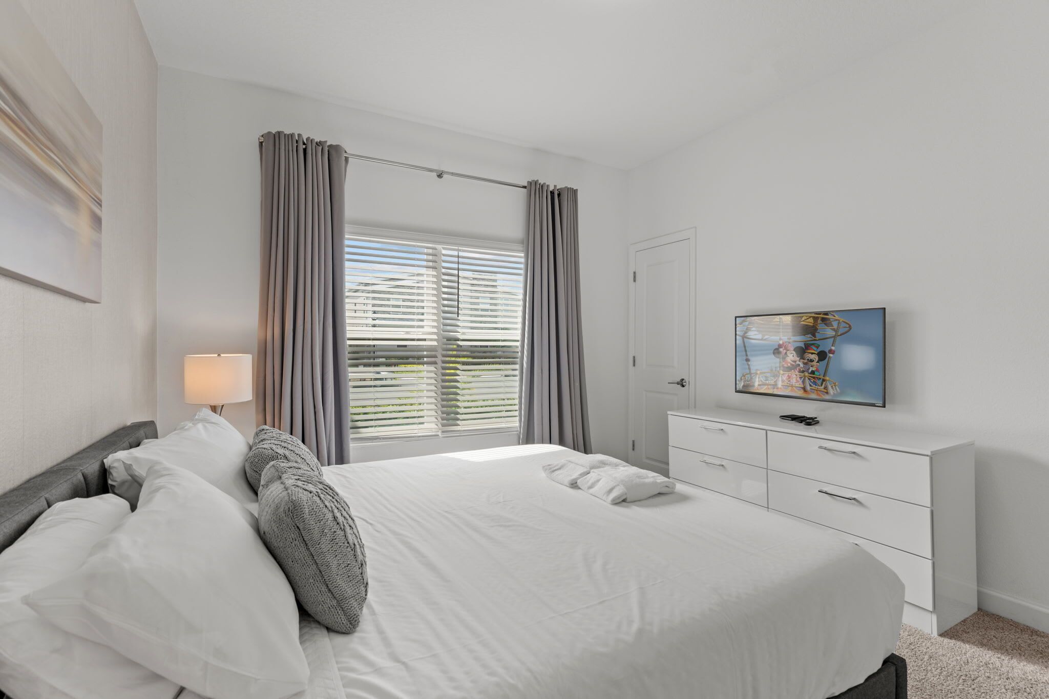 Une chambre à coucher avec un lit, une télévision, une commode et une fenêtre avec des rideaux.