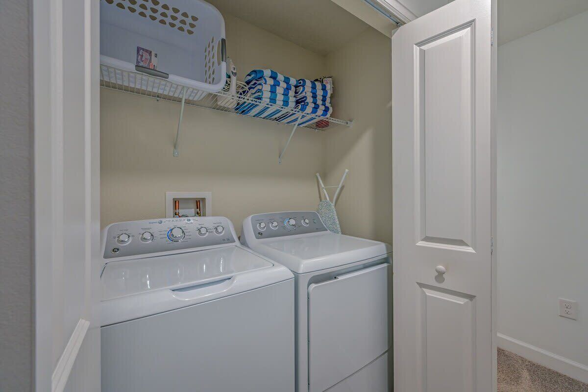 A laundry room with two white washers and dryers, a shelf with folded laundry, and a door.