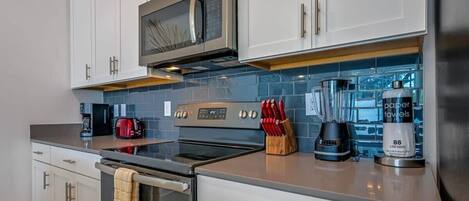 A modern kitchen with white cabinets, stainless steel appliances, a microwave, stove, and a coffee maker.