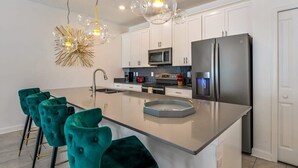 Une cuisine moderne avec des meubles blancs, des appareils en acier inoxydable, un îlot central et des chaises de couleur turquoise.