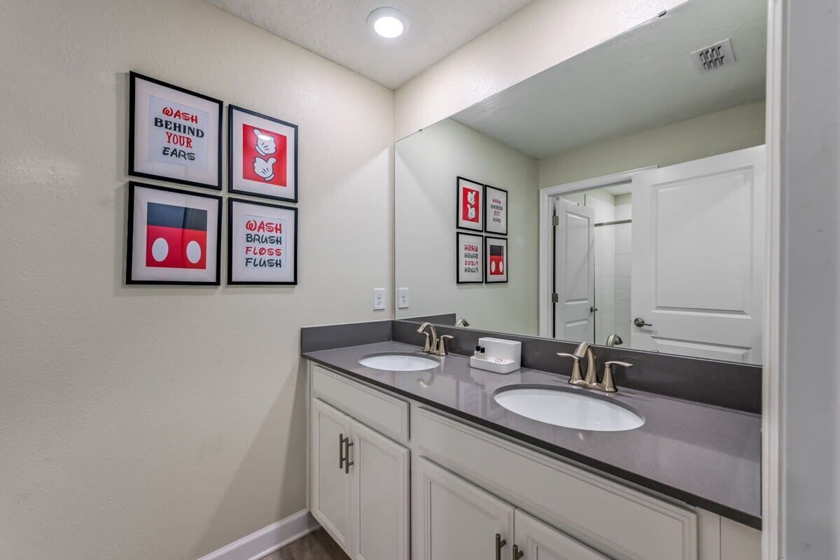 A bathroom with two sinks, a large mirror, and four framed hygiene posters on the wall.