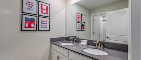 A bathroom with two sinks, a large mirror, and four framed hygiene posters on the wall.