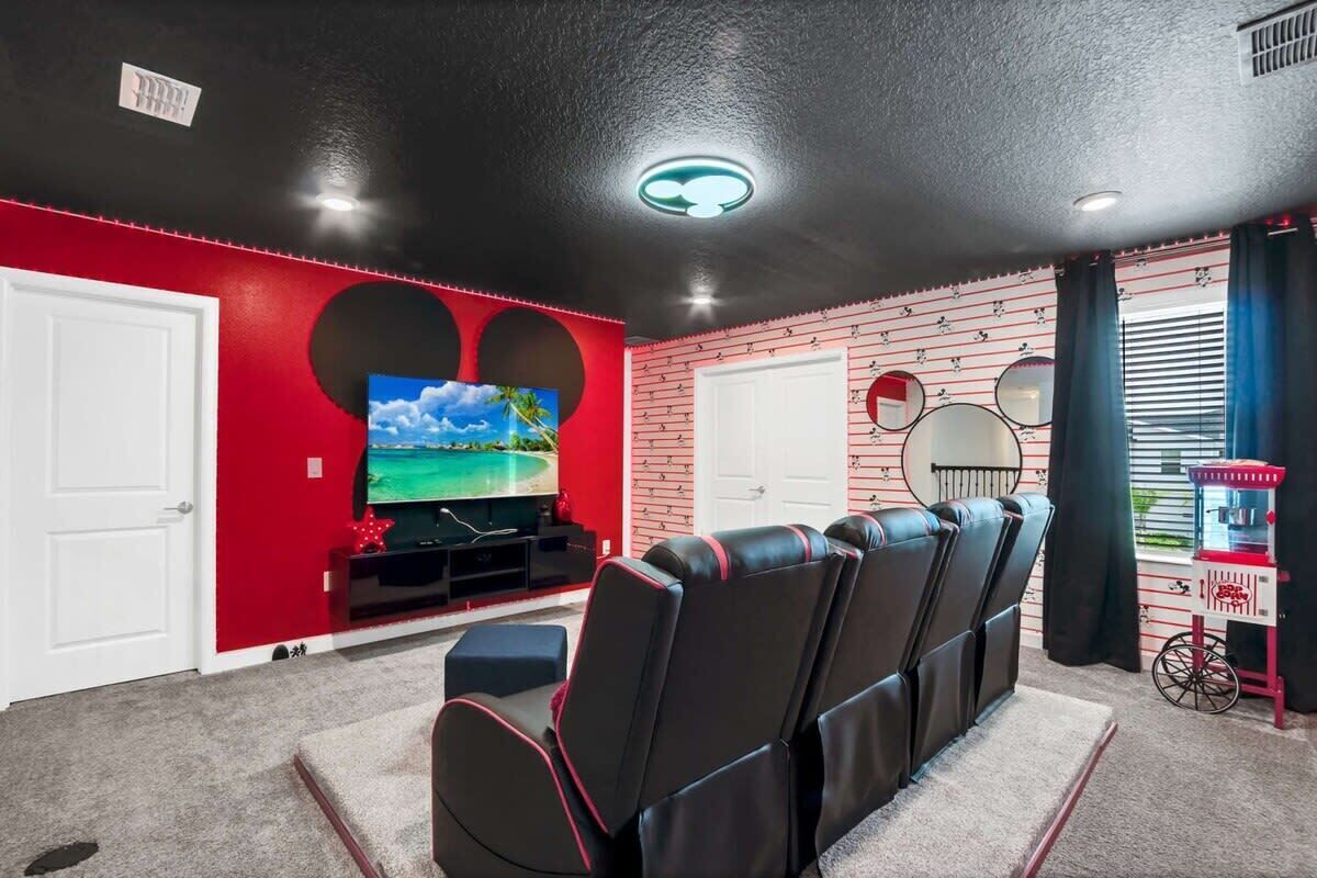 Une salle de cinéma maison avec un mur en briques rouges, un téléviseur à écran plat, des fauteuils inclinables en cuir noir et un appareil à pop-corn.