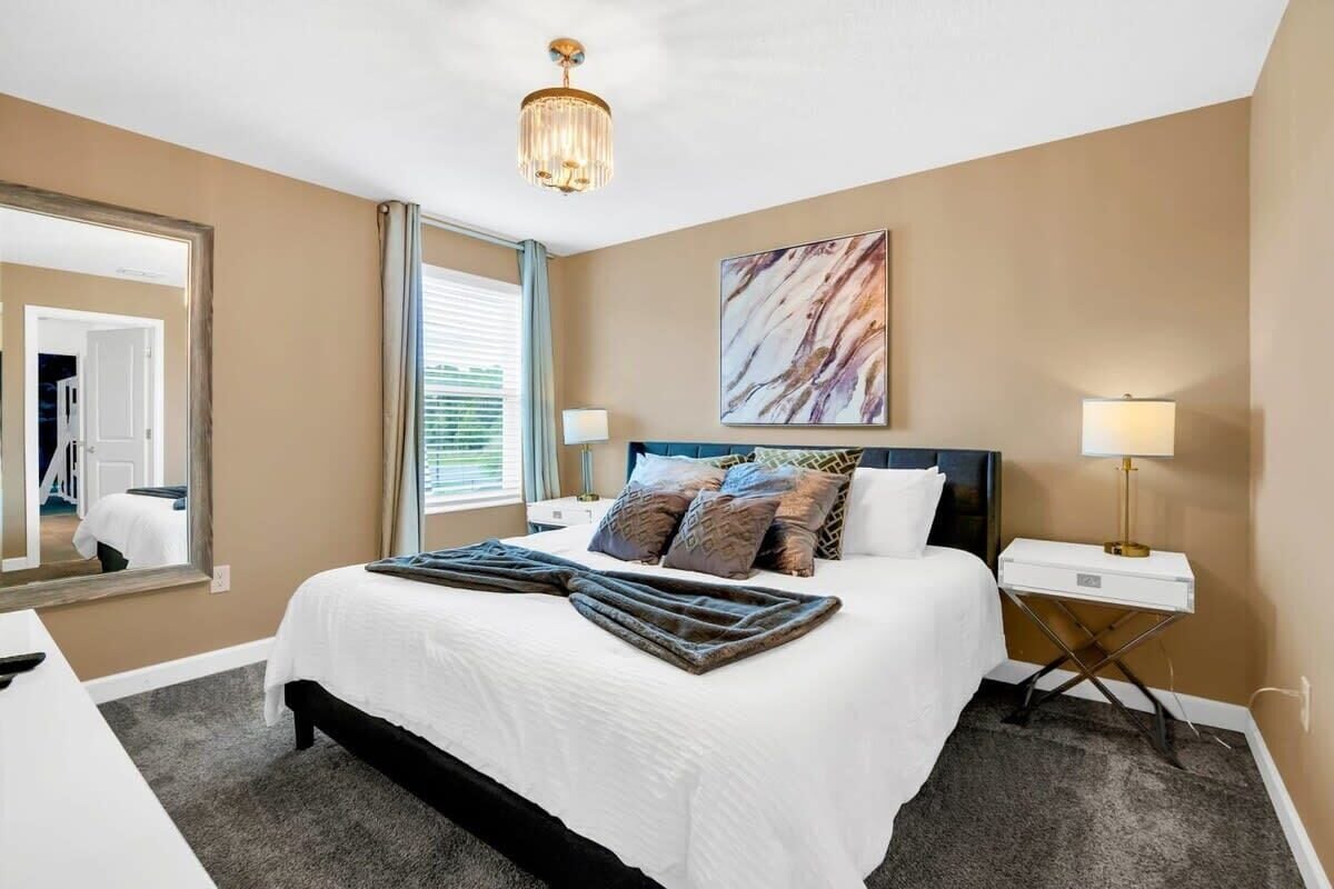 A hotel room with a large bed, bedside lamps, a desk, a mirror, and a ceiling light.