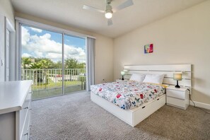 A bedroom with a bed, a desk, a nightstand, a ceiling fan, and a view of the outdoors. - Distinctive Home, Private Pool (Clermont)