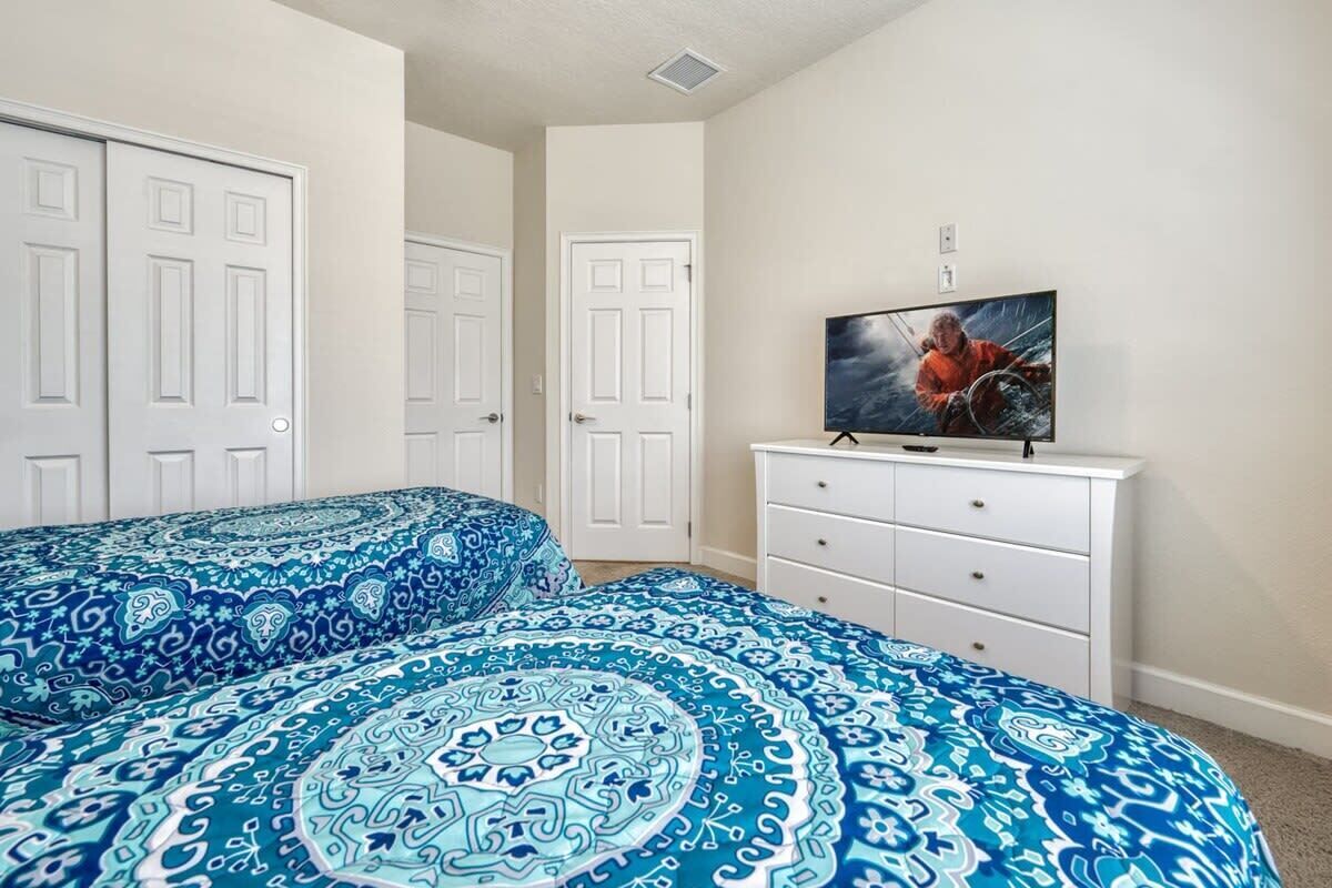 A bedroom with two beds, a television on a dresser, and white doors.