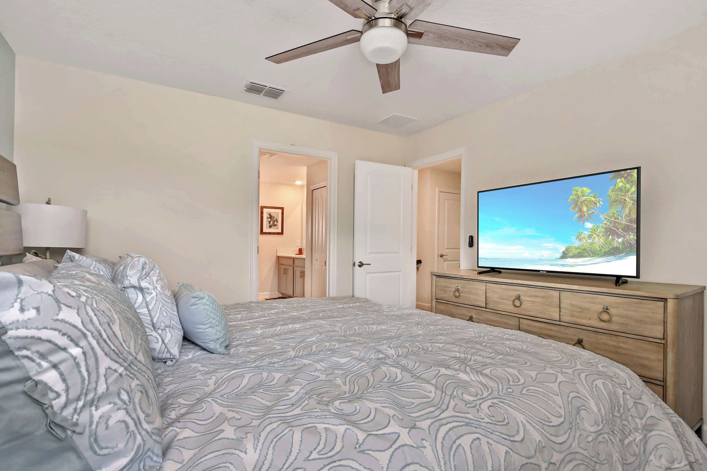 Ein Schlafzimmer mit Bett, Fernseher, Deckenventilator und Kommode.