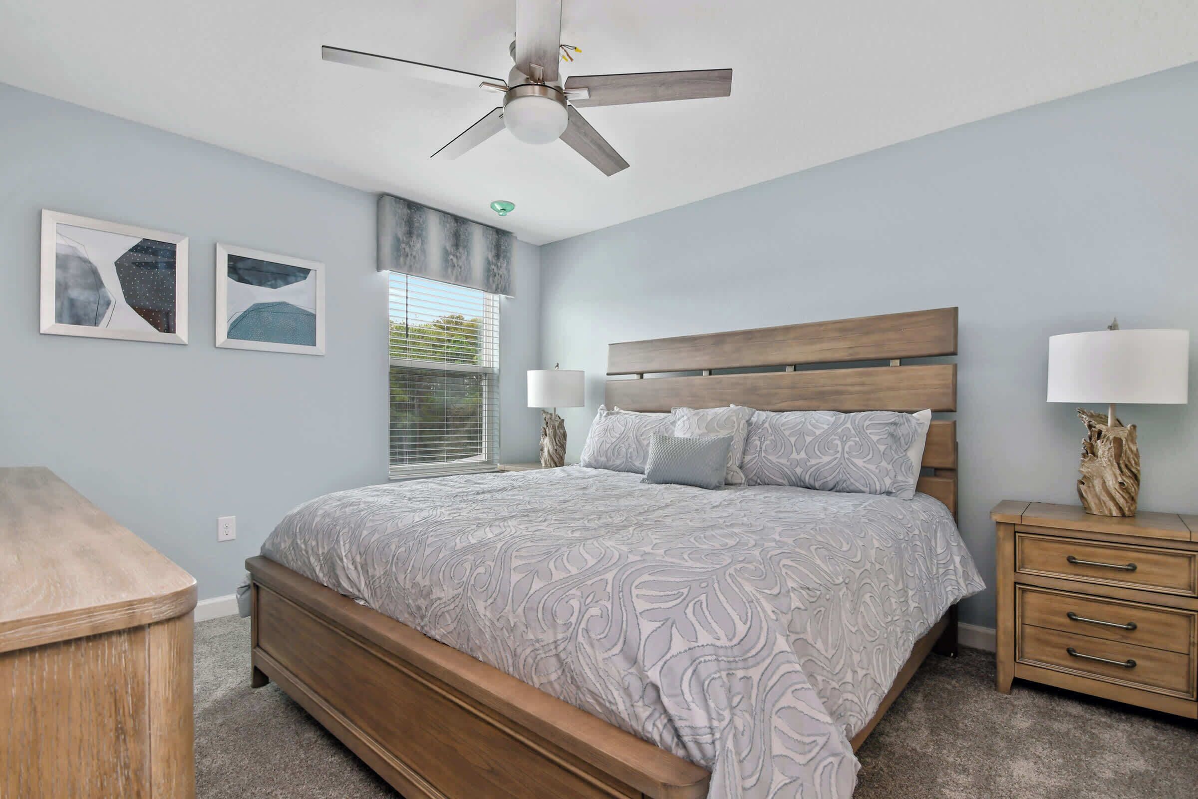 A bedroom with a bed, nightstands, a ceiling fan, and wall art.