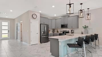 A modern kitchen with grey cabinets, a central island with bar stools, stainless steel appliances, and pendant lighting.