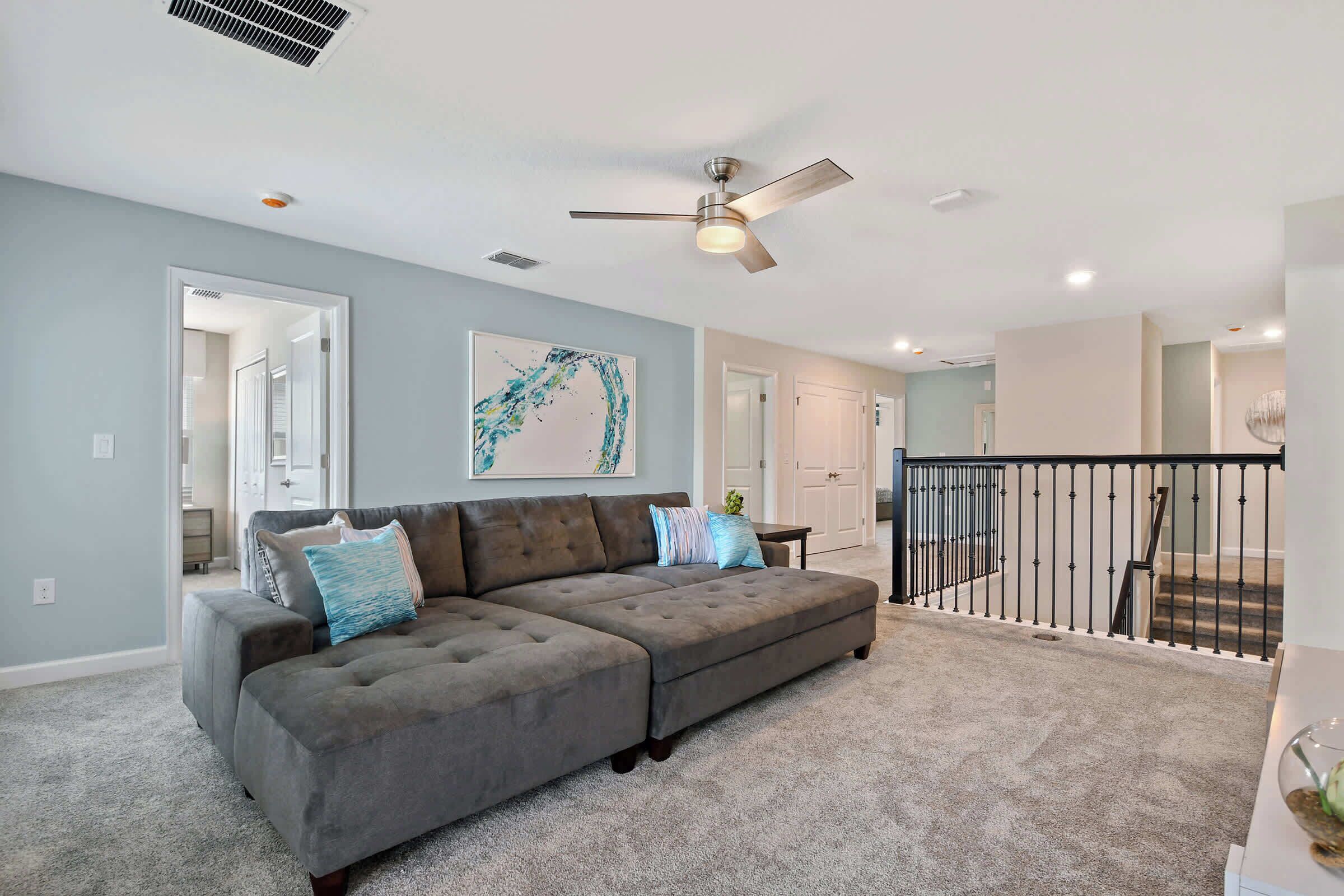 A spacious living room with a large sectional sofa, a ceiling fan, and a view of the upper floor.