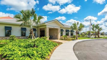 A modern building with a stone facade, a covered patio, and a well-maintained garden with palm trees.