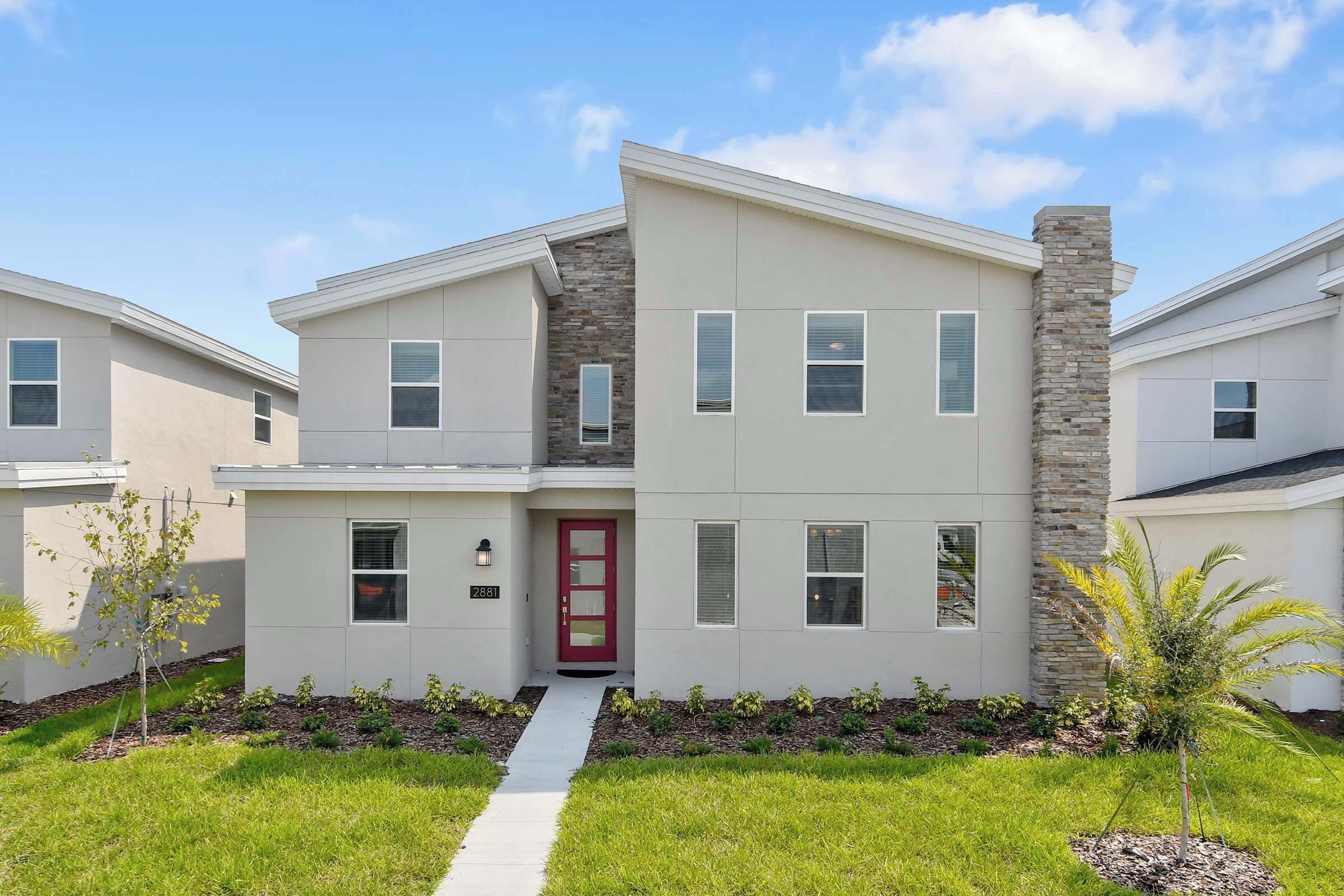 A modern two-story house with a red door, a stone accent wall, and a well-maintained lawn.