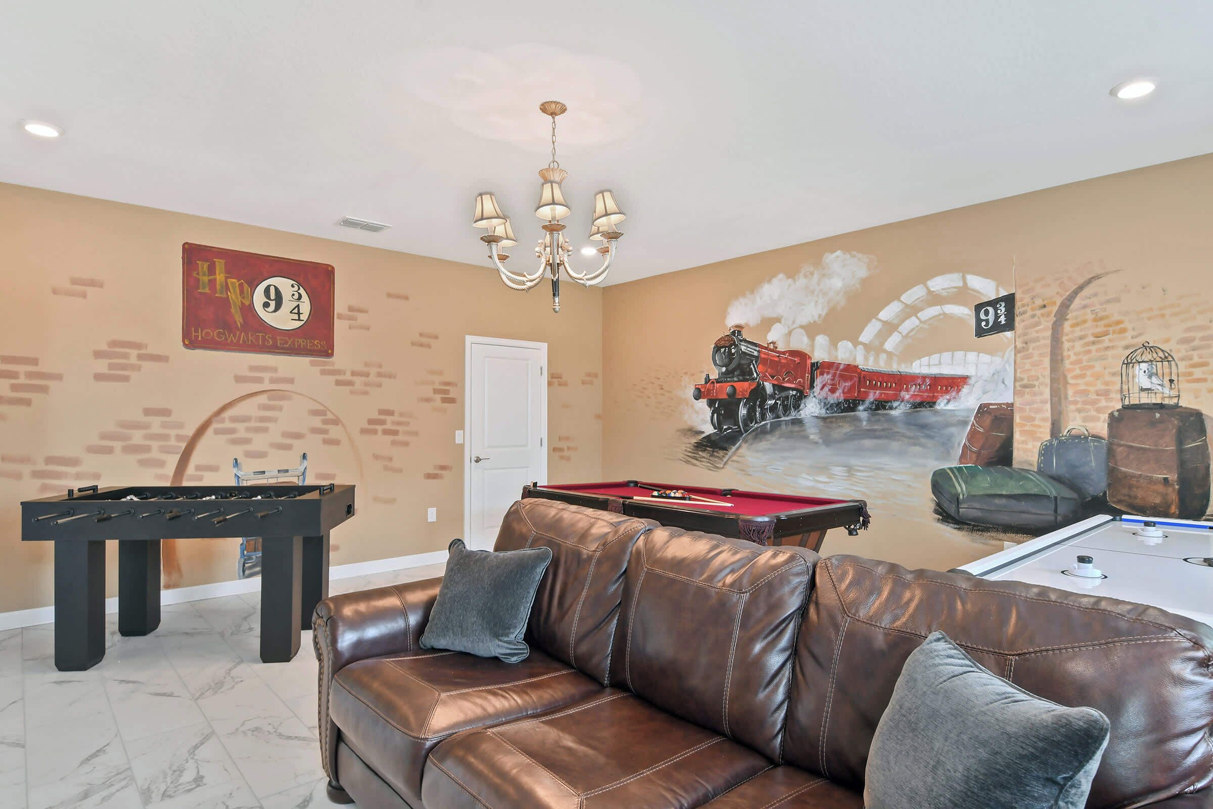 A room with a pool table, foosball table, and a mural of a train.