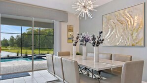 Un espace repas comprenant une grande table, des chaises et donnant sur une piscine.