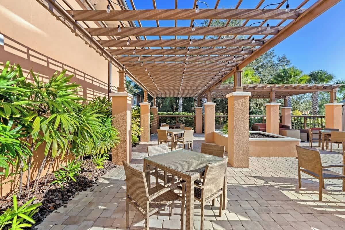 Un patio al aire libre con mobiliario de mimbre, una pérgola con luces colgantes y diversas plantas.