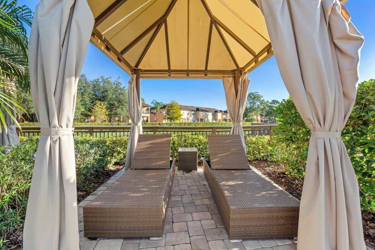 Ein überdachter Außenbereich mit Korlounge-Stühlen und einem zentralen Tisch, umgeben von Grünpflanzen und mit Blick auf Gebäude im Hintergrund.