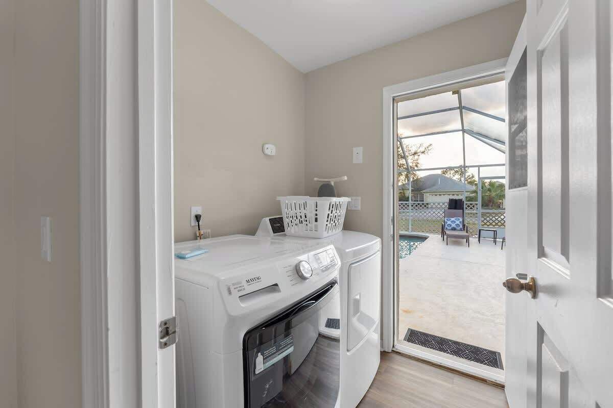 A laundry area with a front-loading washer and dryer, a basket, and a small table with a chair outside.