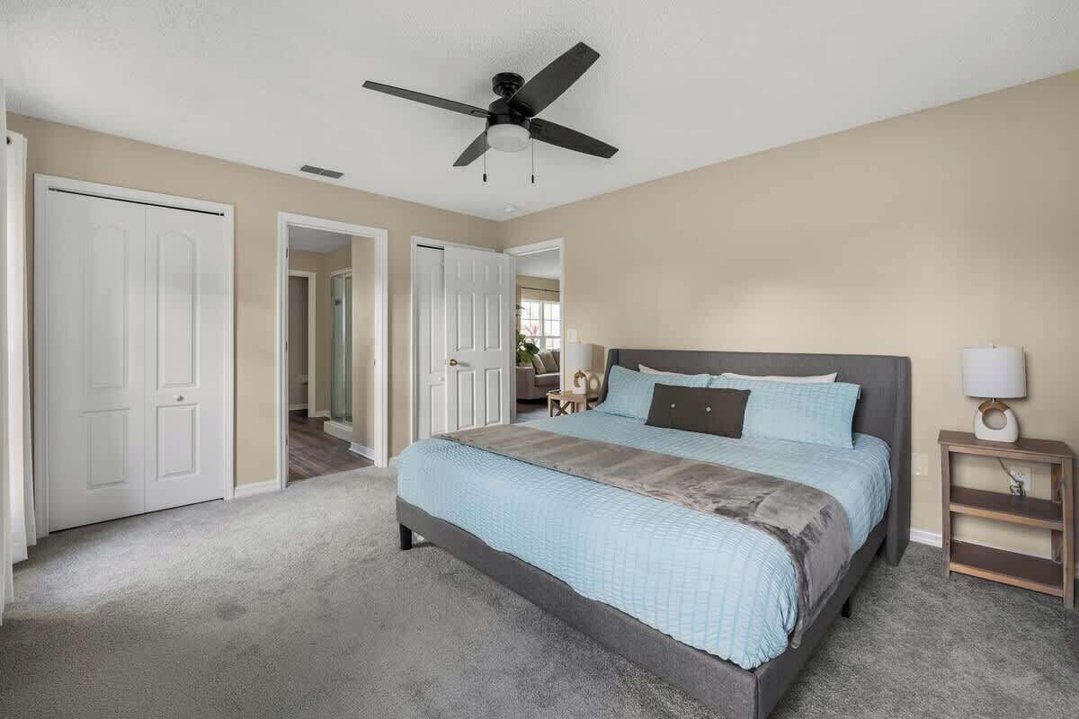 A bedroom with a bed, a ceiling fan, a nightstand, and a door leading to another room.