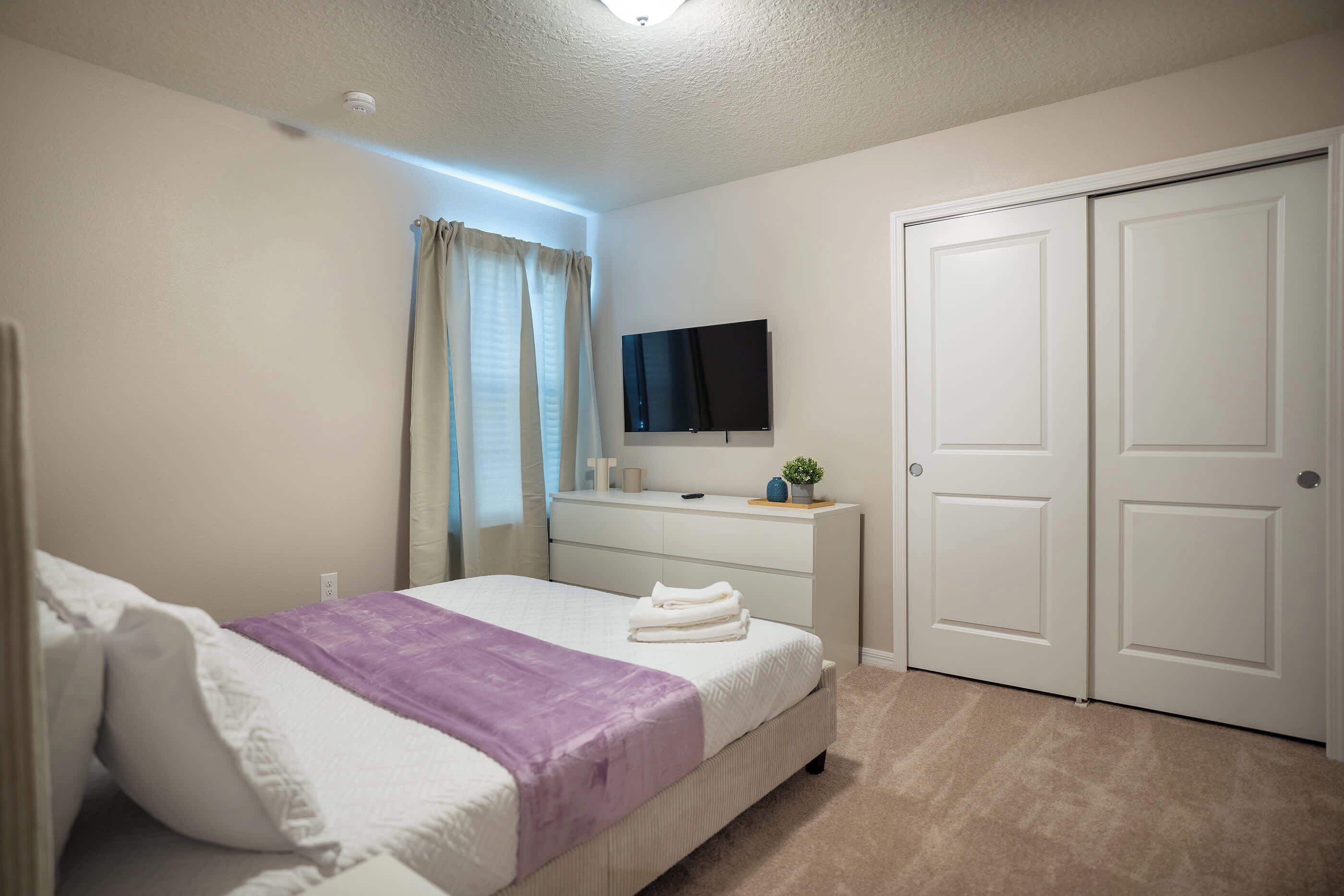 A bedroom with a bed, a dresser, a television, and a closet.
