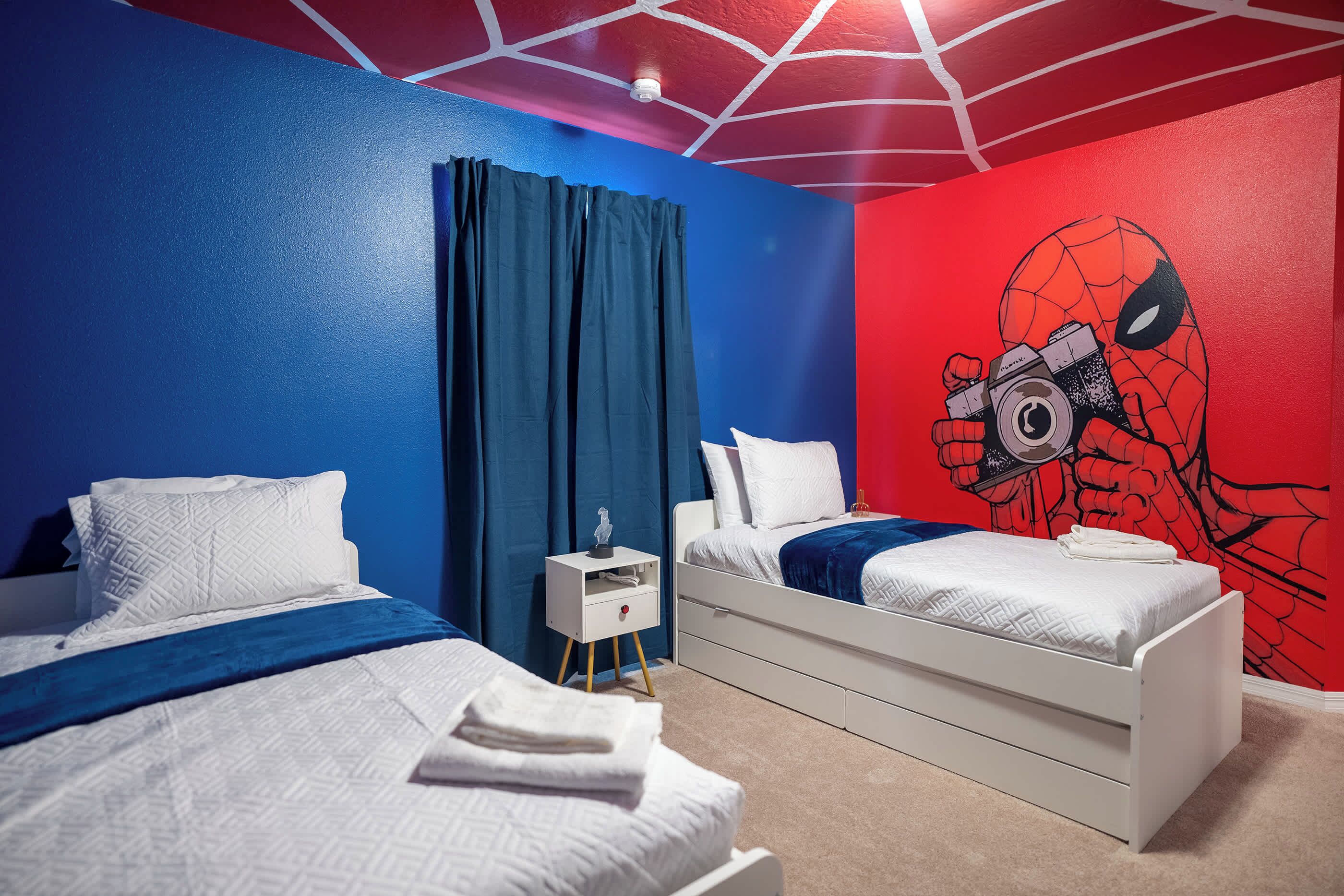 A bedroom with two beds, a nightstand, and a Spider-Man mural on the wall.