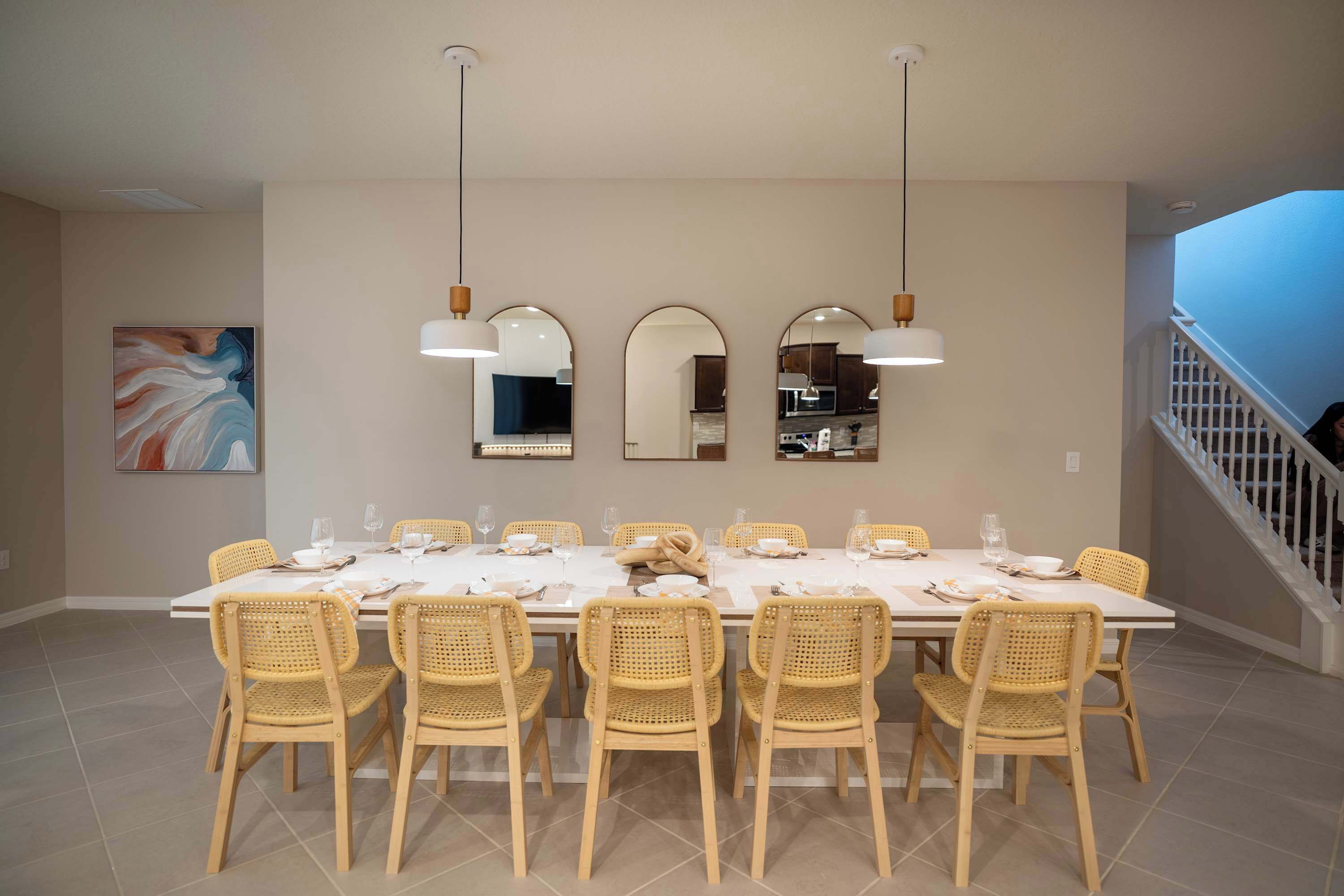 A dining area with a long table, wicker chairs, and pendant lights.