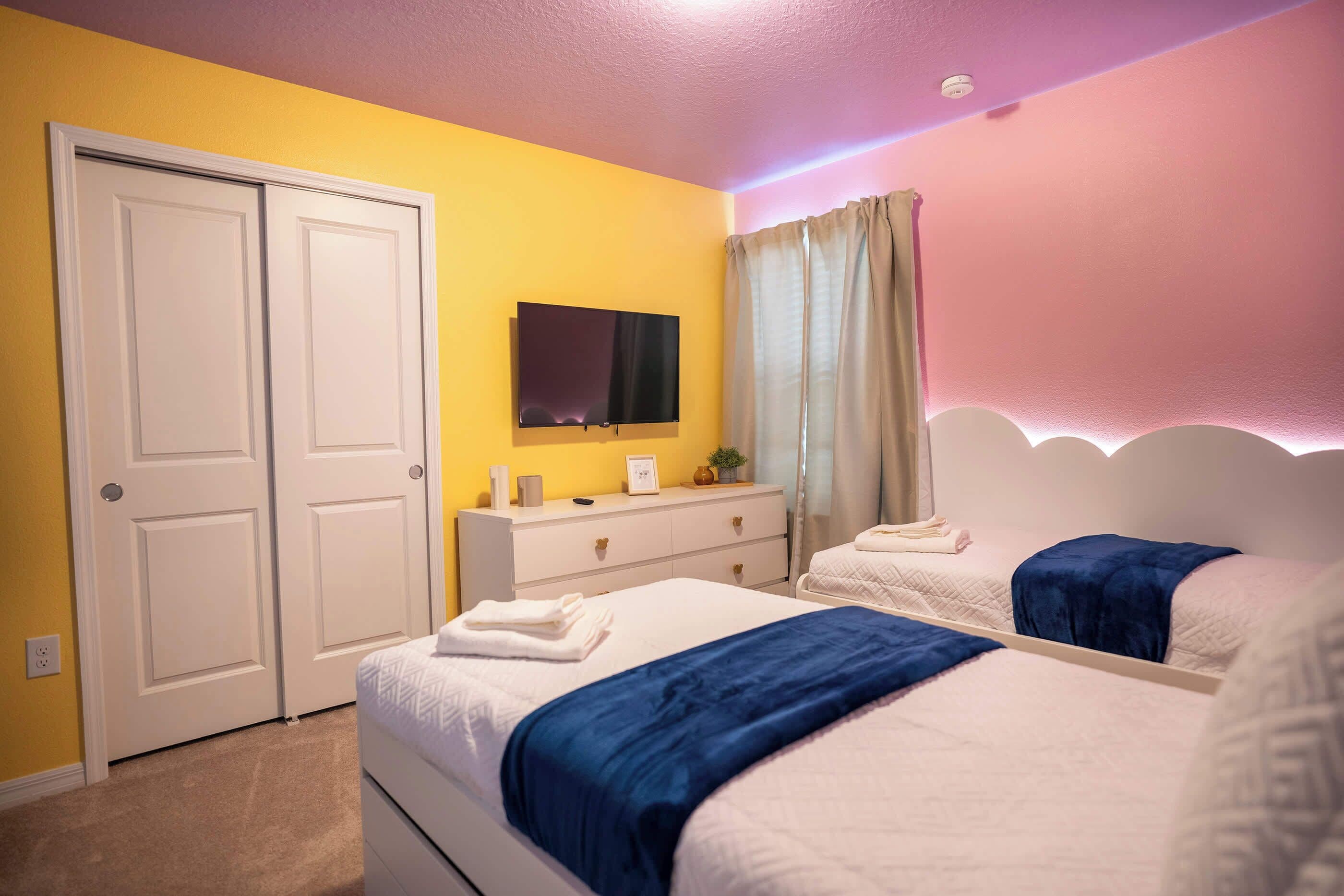 Une chambre avec deux lits, une commode, une télévision et une porte.
