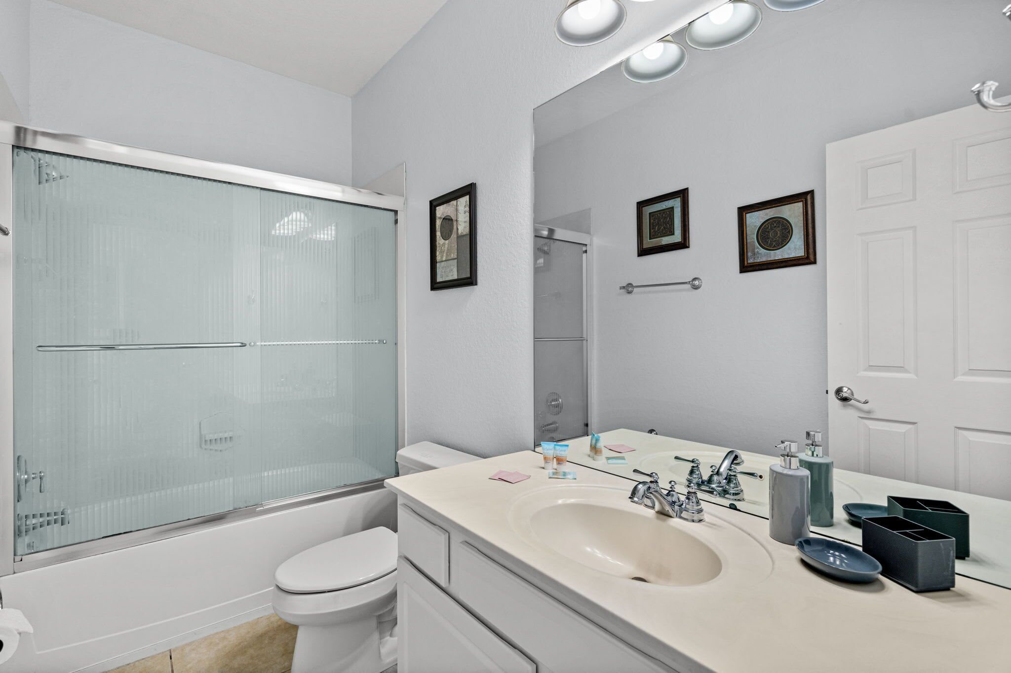 A modern bathroom with a glass shower enclosure, a white toilet, a large sink with a mirror, and a white door.