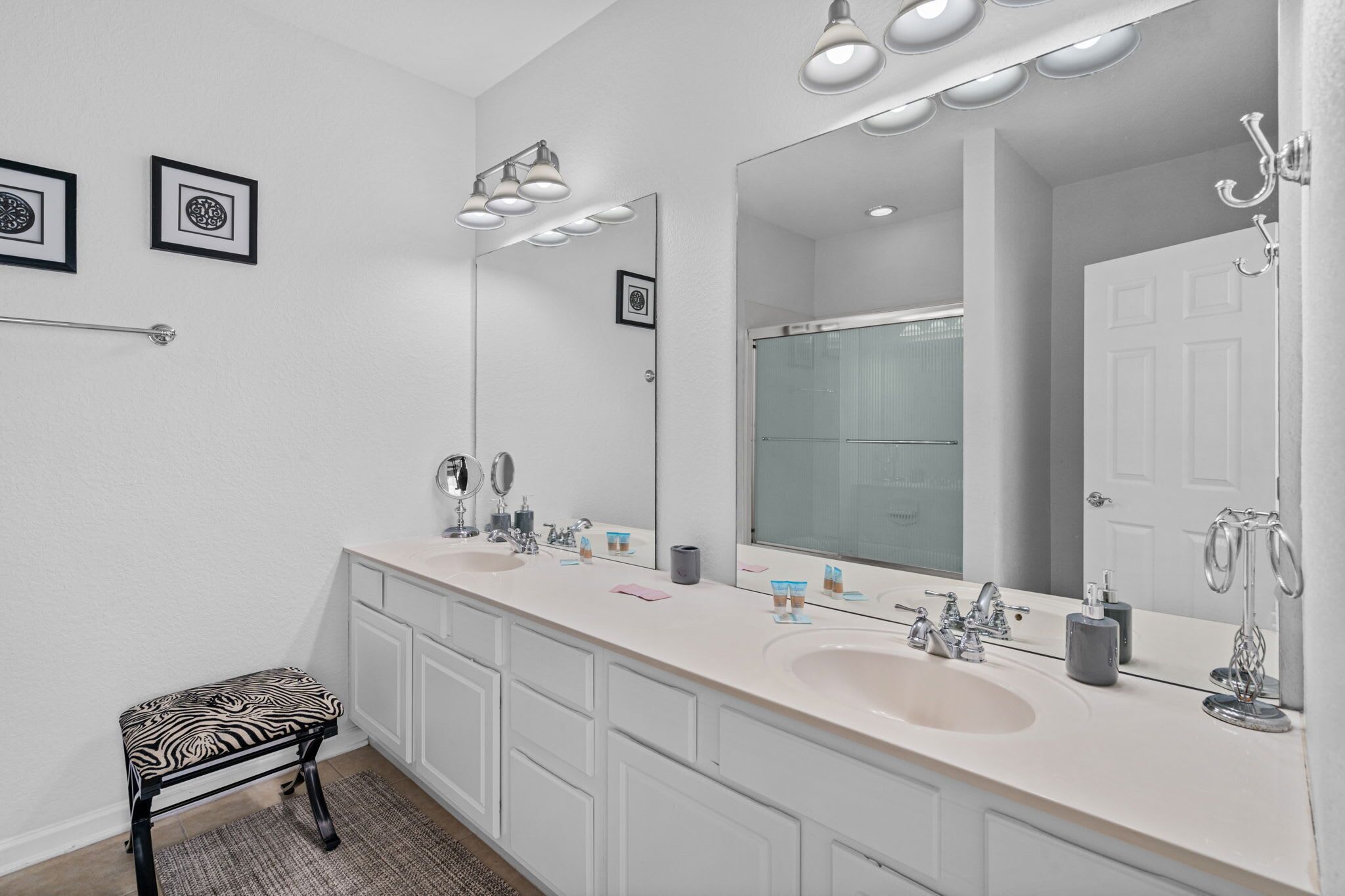 Une salle de bain moderne avec deux vasques, un grand miroir et un banc à motifs zébrés.