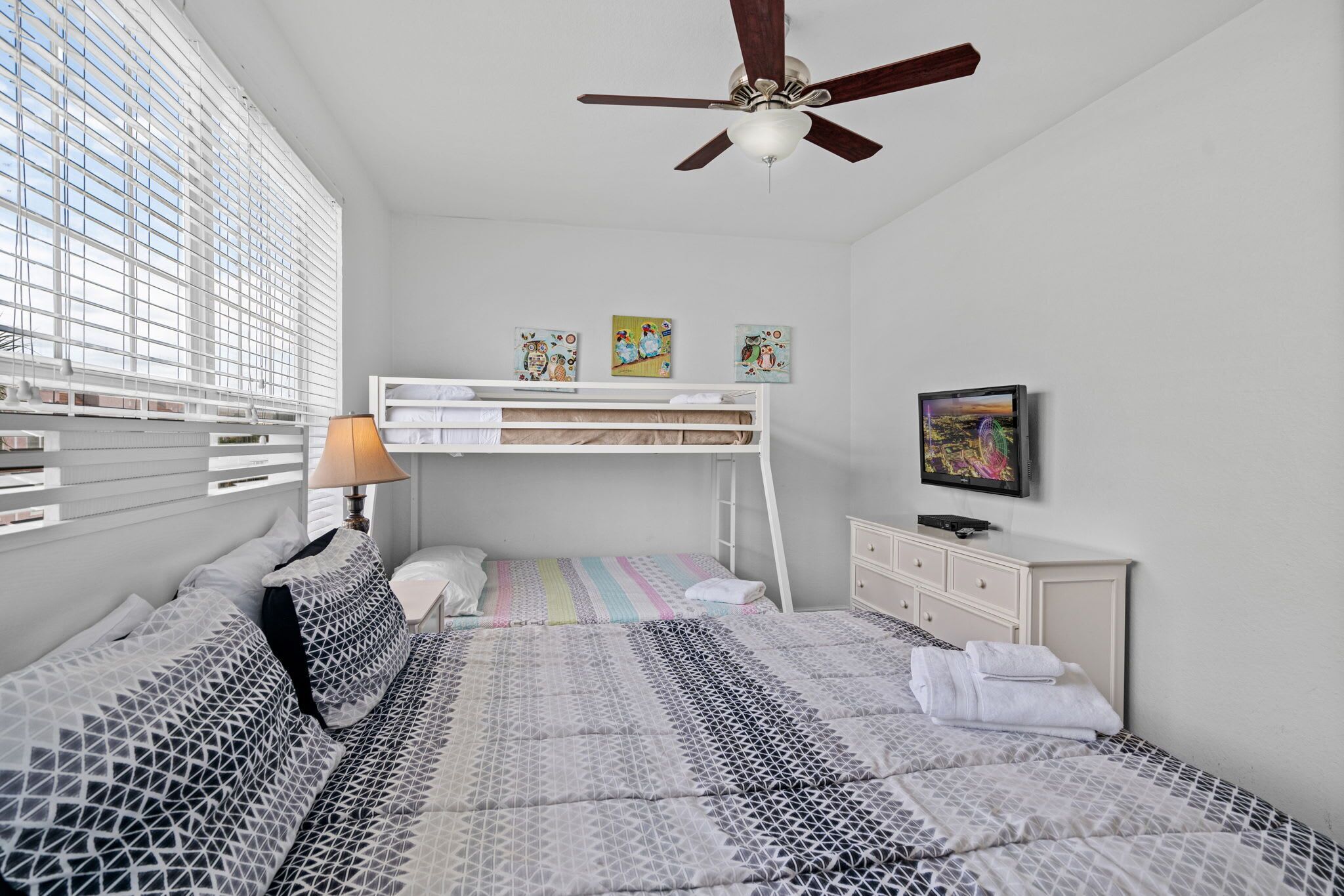 Une chambre avec un lit superposé, un bureau, une chaise, une lampe et un téléviseur.