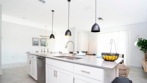 A modern kitchen with white cabinetry, a central island, and pendant lighting. - Comfy Themed Home, Private Pool, Prime Location (Davenport)