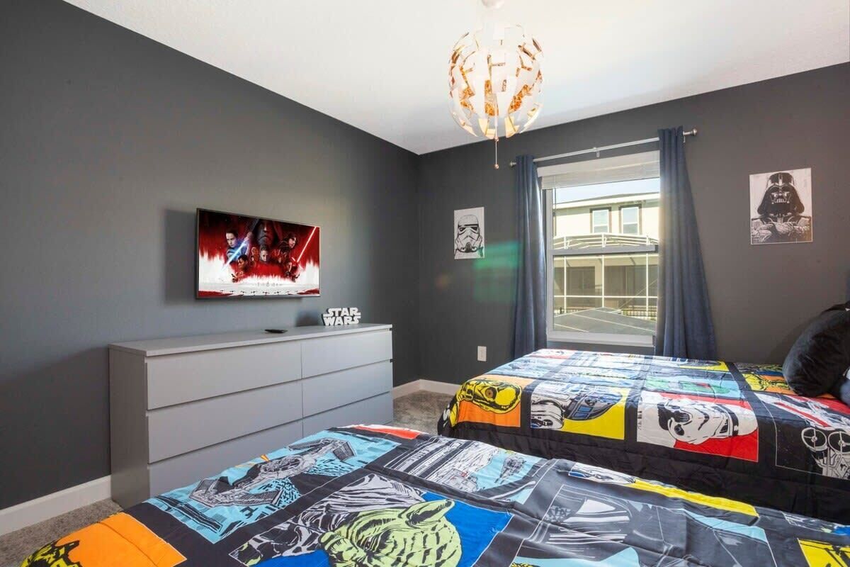 A bedroom with a Star Wars themed bedspread, a television on the wall, and a Star Wars poster.