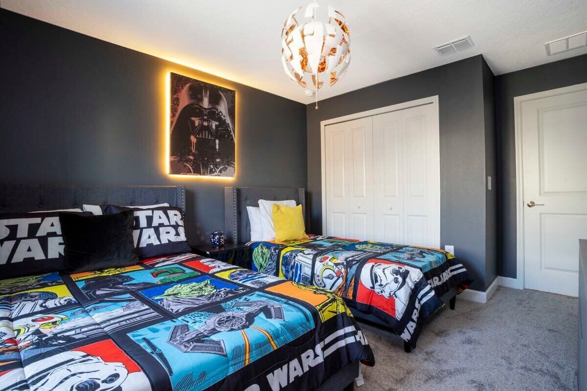 A bedroom with two beds, Star Wars themed bedding, a Darth Vader poster, and a modern chandelier.